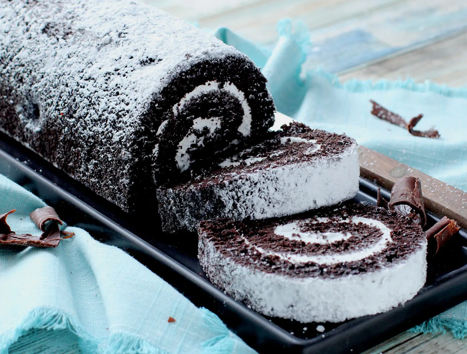 Chocolate Crème Cake roll and slices on cutting board next to chocolate shavings