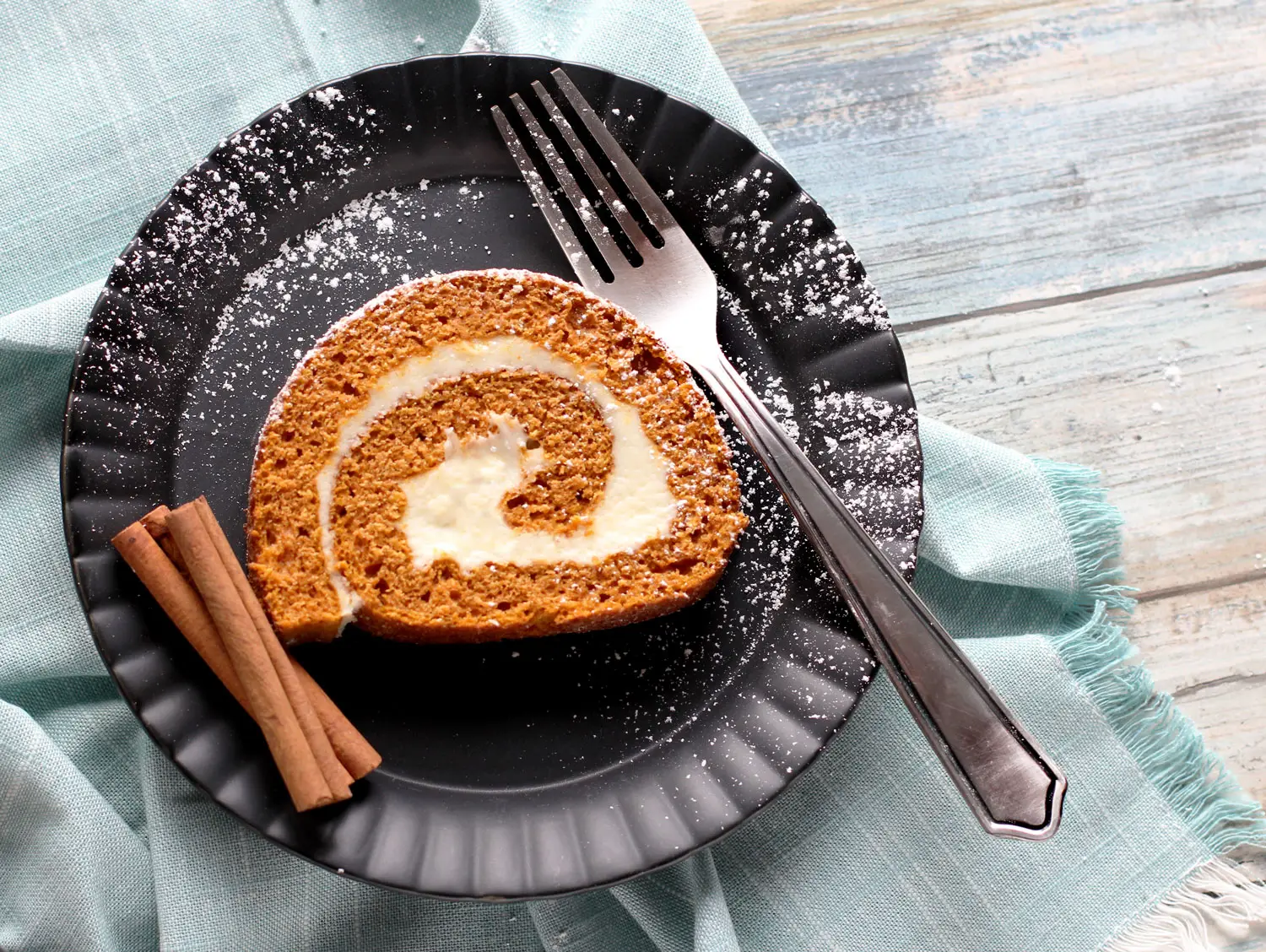 Pumpkin cake roll slice on plate with fork and cinnamon sticks