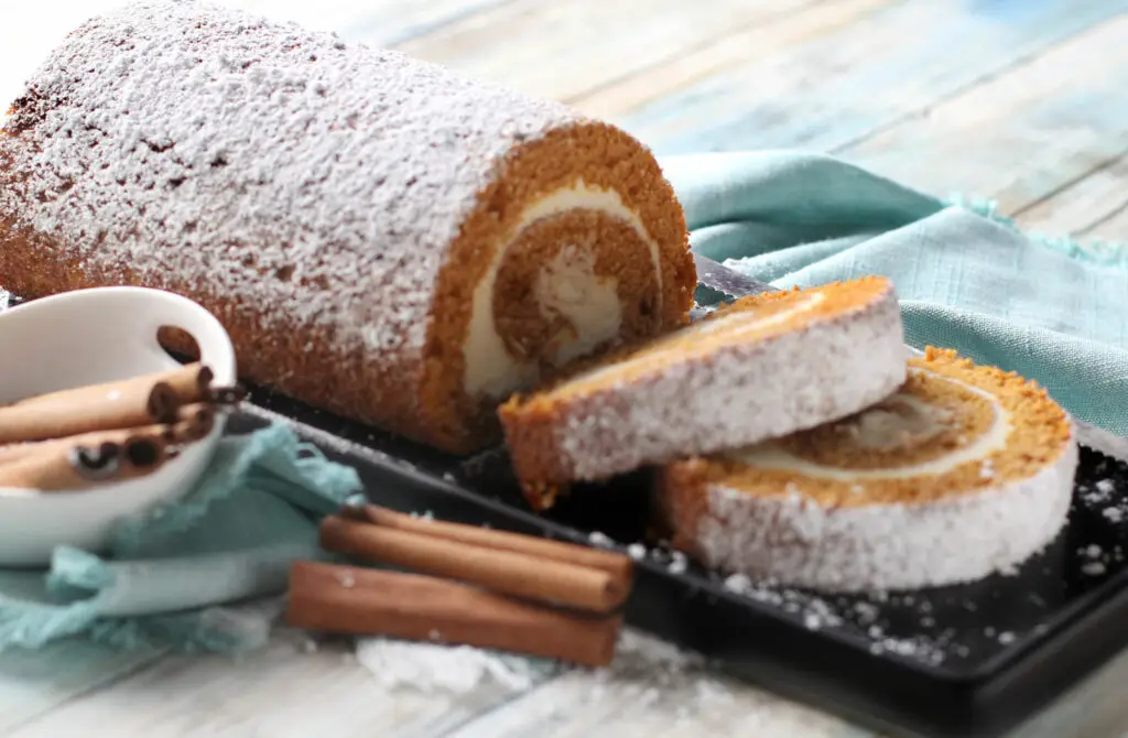 Pumpkin cake roll slice on cutting board next to bowl of cinnamon sticks