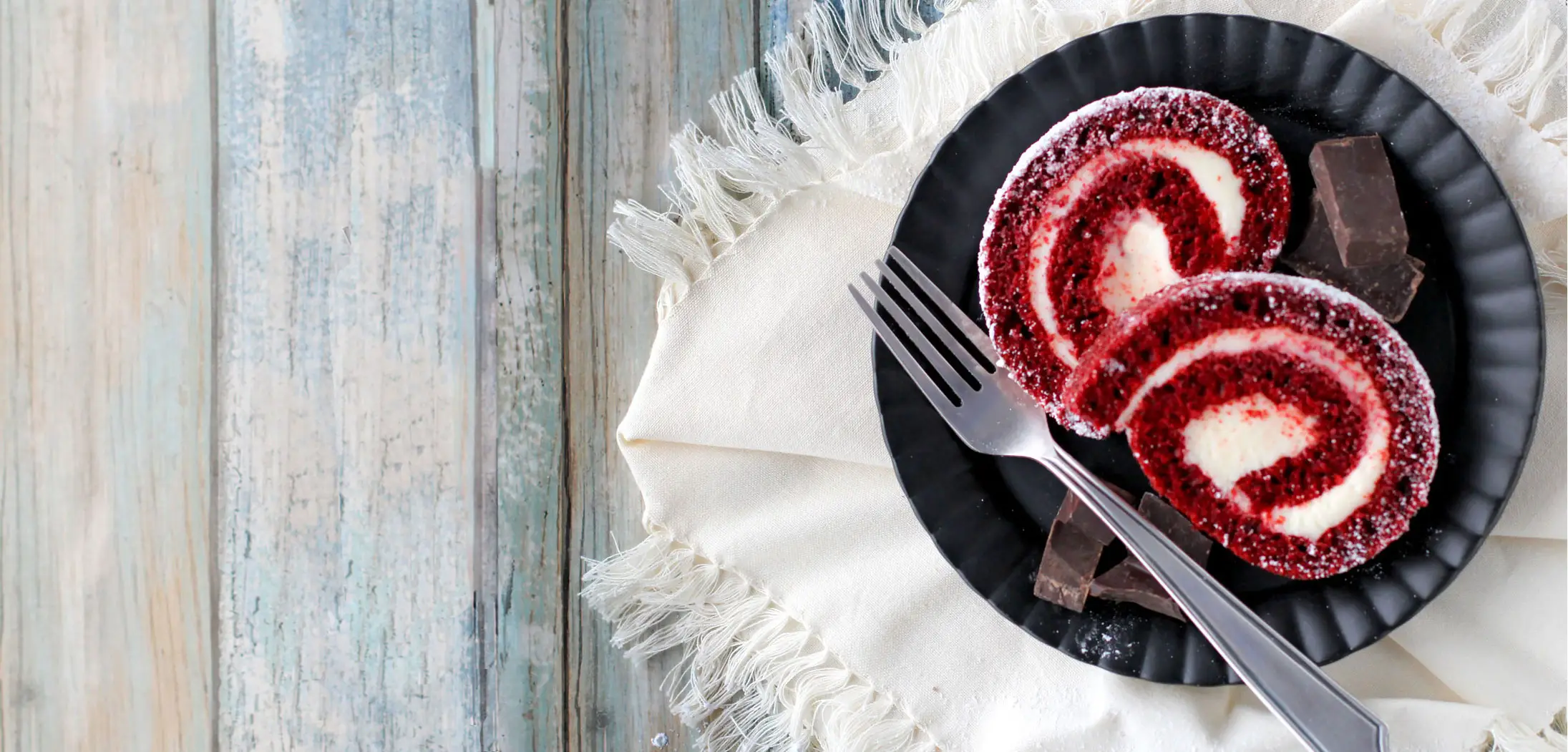 Two red velvet cake roll slices on plate with fork and chocolate pieces