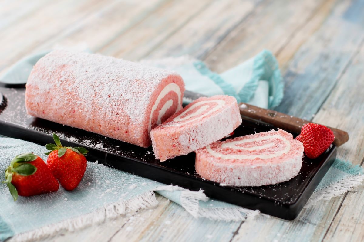 Strawberry Cheesecake Cake Roll with strawberries and knife on cutting board