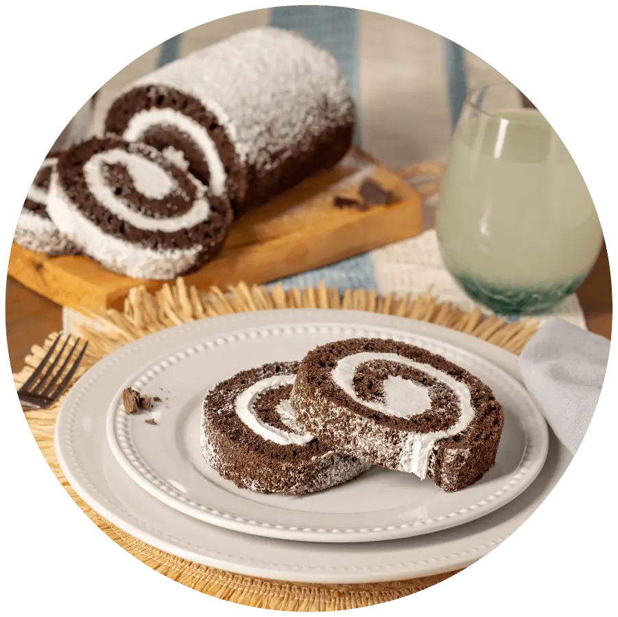 Joyful Traditions Chocolate Creme Cake Roll - two slices on a plate with the full cake roll on a cutting board in the background.