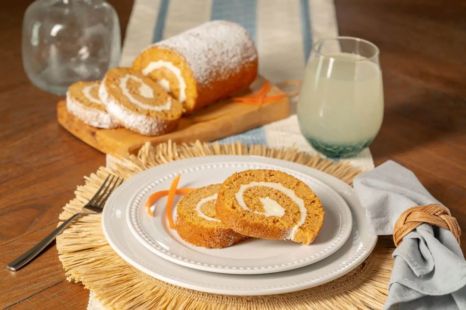 Joyful Traditions Carrot Cake Cake Roll - two slices on a plate with the full cake roll on a cutting board in the background.