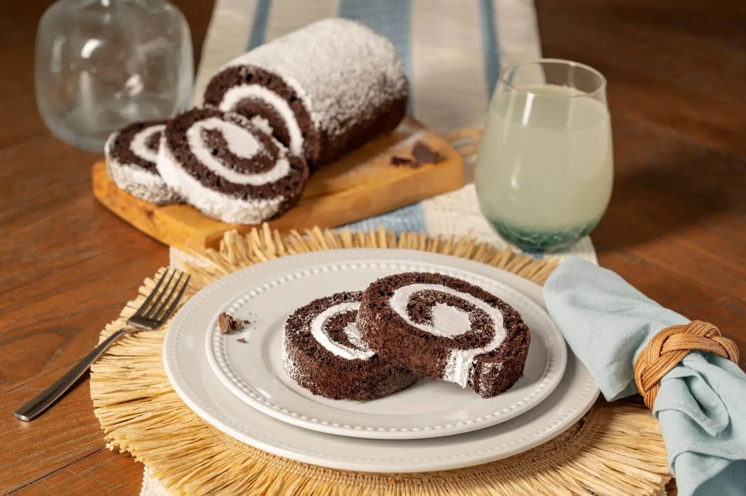 Joyful Traditions Chocolate Creme Cake Roll - two slices on a plate with the full cake roll on a cutting board in the background.